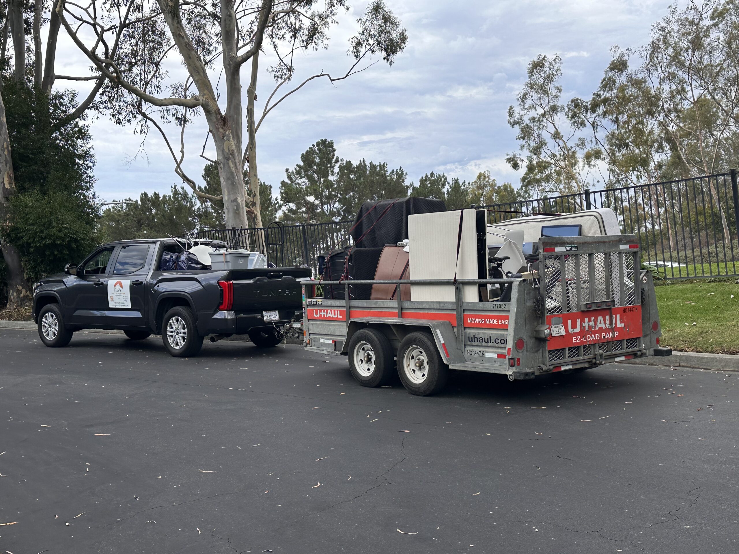 Pickup truck with attached trailer loaded with furniture and boxes, secured with moving blankets and straps.